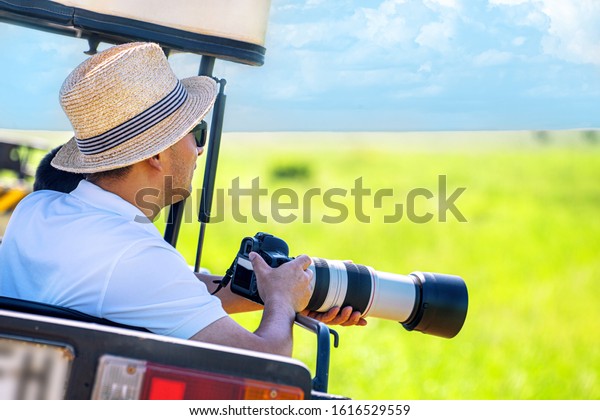 The man photographer takes a picture\
with professional camera from touristic vehicle on tropical safari.\
Wildlife photography in Kenya,\
Tanzania.