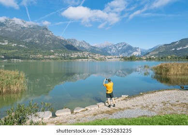 Man photographs a beautiful lake on a splendid sunny day. Lake Annone or lake Oggiono, Italy. Panorama from the cycle pedestrian path near Annone di Brianza town. In the background the town of Civate - Powered by Shutterstock