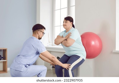 Man physiotherapist or nurse helping fat overweight woman in doing sport exercises with fit ball holding her knees. Physiotherapy, rehab, caregiver support and nursing help concept. - Powered by Shutterstock