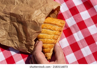 Man Picking An Apple Turnover In A Brown Paper Bag Outdoors On A Gingham Cloth. Environmentally Friendly Recycle Packaging