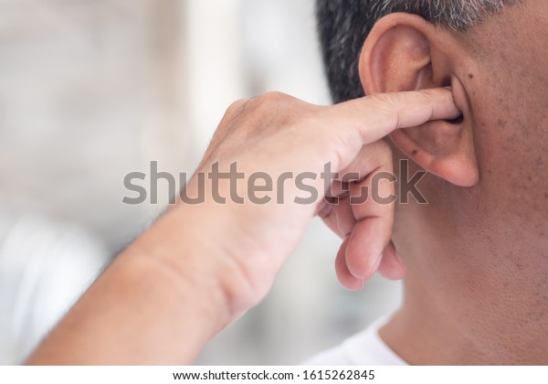 man picking his ear with nasty, dirty habit; concept\
of ear wax picking, unhealthy habit, bad manner with smelly, stinky\
ear wax