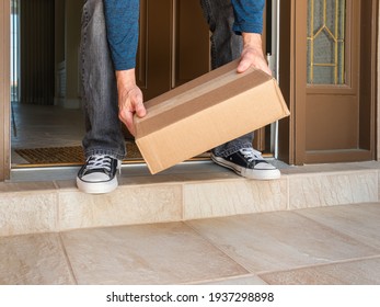 Man picking up a package box delivered to a residential doorstep. Online order package delivery to the front porch of home.
