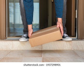 Man Picking Up A Package Box Delivered To A Residential Doorstep. Online Order Package Delivery To The Front Porch Of Home.