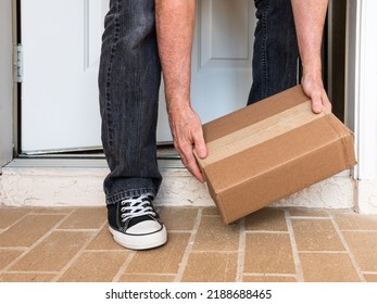 Man Picking Up A Package Box Delivered To A Residential Doorstep. Online Order Package Delivery To The Front Porch Of Home.