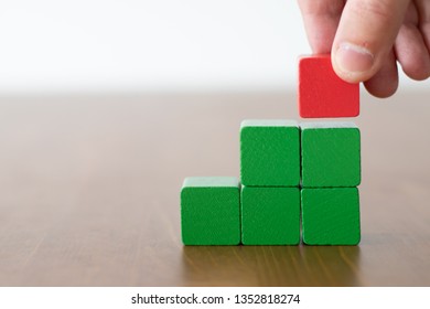 Man Picking Up A Single Red Cube On Top Of A Group Of Green Wooden Cubes 