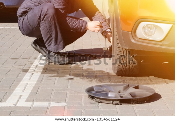 Man picks up car jack to change tire. Car tires\
and wheels with wheels. Car service. Change a flat car tire on\
road. Man is changing\
tires.