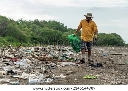 Man picks up plastic garbage on beach in the morning, Panama, Central America.