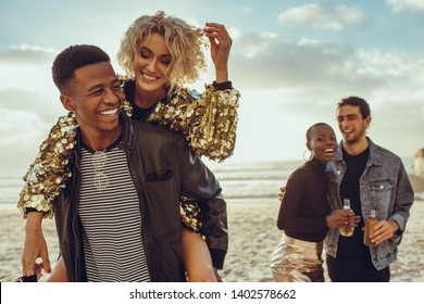 Man piggybacking woman with friends walking at the beach. Multiracial friends enjoying themselves on their beach holiday.