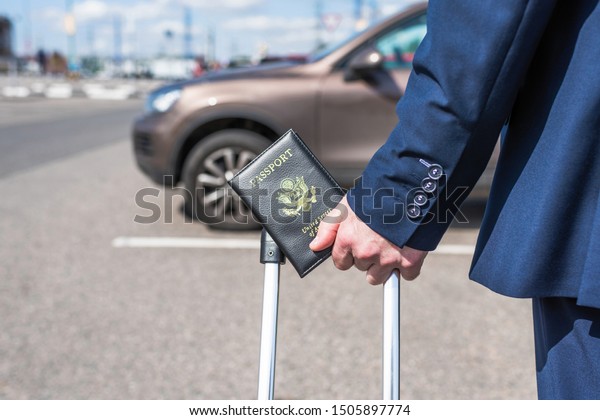 Man pilot in a blue\
uniform (suit), suitcase and american passport. airport parking\
rental car. concept