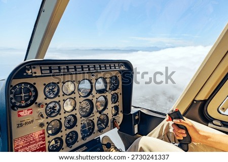 Man pilot operating helicopter control panel and joystick during flight, high above clouds. Luxury Cape Town tour. Aircraft cockpit view.