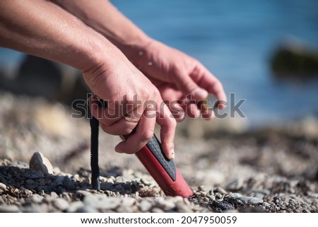 Man with a pin pointer metal detector on the sea beach is looking for the lost coins. Summer hobby.
