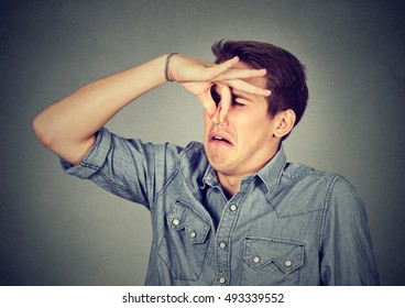 Man Pinches Nose With Fingers Looks With Disgust Something Stinks Bad Smell Isolated On Gray Background. Human Face Expression Body Language Reaction