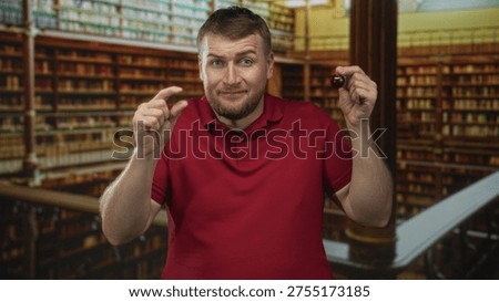 Man pinches a tiny gap between fingers while holding a cherry in a library building; curiosity smallness tease.