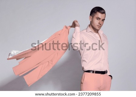 A man in a pink suit and a fashionable pink shirt isolated on a gray background. A man in a Barbie outfit.