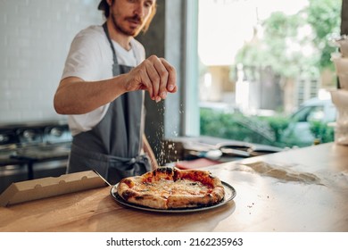 Man pizza master prepares pizza according to customer requests. Process of placing ingredients on a pizza. Sprinkling cheese on a pizza. - Powered by Shutterstock