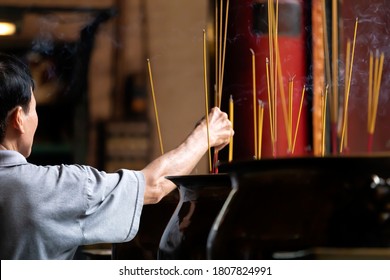 A Man Places Burning Incense Sticks At An Altar In An Old Chinese Buddhist Temple In Southest Asia