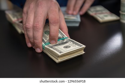 Man Placing A Bet, Making Payment Or Offering A Bribe Passing Over A Large Stack Of 100 Dollar Bills In A Close Up View On His Hand