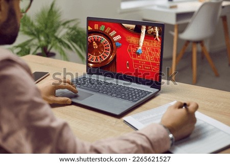 Man placing bets and writing notes while playing online casino at home on his laptop. Close up of laptop screen on which roulette is being played and which man addicted to gambling is looking at.
