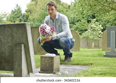 Man Placing Flowers By Headstone In Cemetery