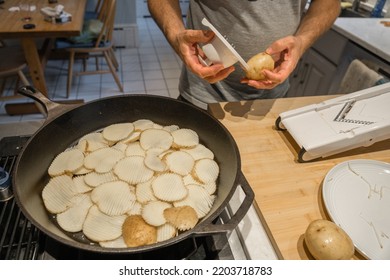 Man Placing Ridged Slices Of Raw Potato Into Frying Pan After Slicing Them With A Mandolin In Home Kitchen.