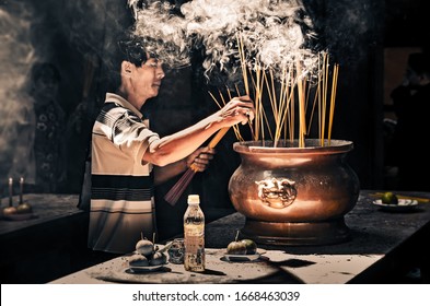 Man Placing Smoking Incense Sticks In A Pot In The Asian Temple Of Thien Hau. (Ho Chi Minh City, Vietnam - 25/01/2020)