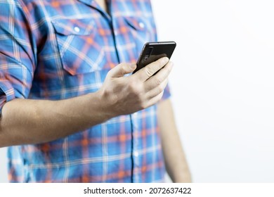 A man in a plaid shirt holds a black mobile phone in his hand on a white background - Shutterstock ID 2072637422
