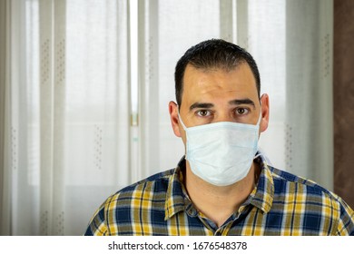 Man In Plaid Shirt And Mask By Covid-19 Virus In The Living Room At Home