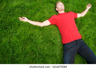 Man in plain red T-shirt with copy space lying outdoors with arms spread in a patch of lush grass