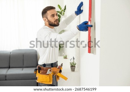 man plasterer construction worker at work, takes plaster from bucket and puts it on trowel to plastering the wall, wears helmet inside the building site of a house