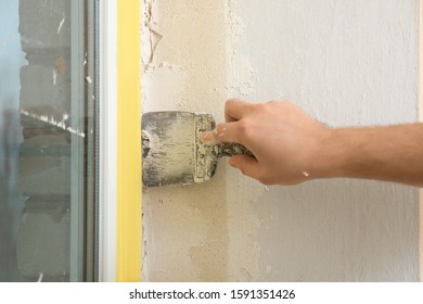 Man Plastering Window Area With Putty Knife Indoors, Closeup. Interior Repair