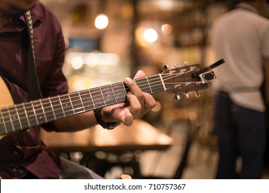 Man playing acoustic guitar in the bar at night shot with high iso with blur background - Powered by Shutterstock