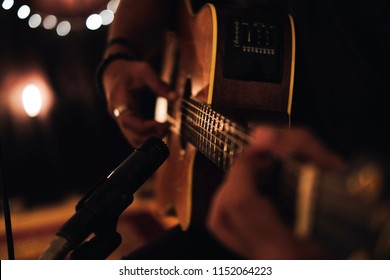 A man playing acoustic guitar in recording session with microphone and beautiful lighting