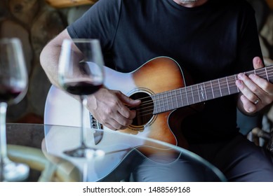 Man Playing Acoustic Guitar With Wine Glasses In Foreground