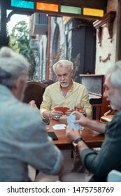 Man Playing Cards. Grey-haired Bearded Man Playing Cards With Friends While Sitting Outside The Pub