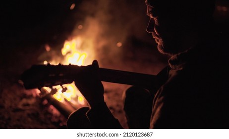 Man is playing guitar by the campfire in nature. Weekend in nature by the fire. Adult man is resting in forest near fire at night.	