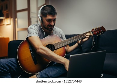 Man Playing Guitar Lessons Online At His Home. Evening Scene