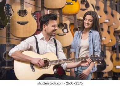 Man Is Playing Guitar Near Young Girl On A Background Of Guitars In The Music Store.