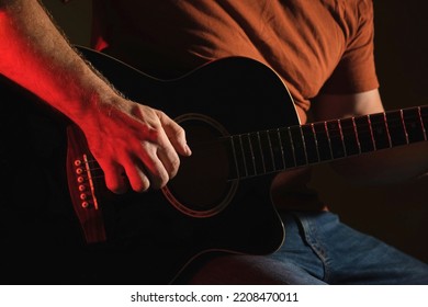 Man Playing Guitar with Neon Light. Unrecognizable Person Rehearsing. Strumming Acoustic Guitar. Musician Plays Music. Male Fingers and Fretboard Close Up. Man Hand Playing Guitar Neck in a Dark. 4K