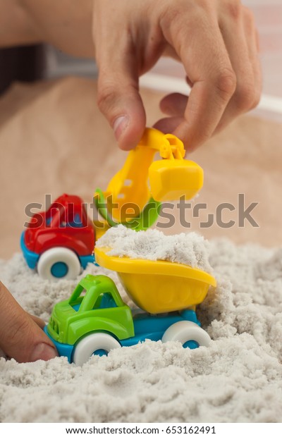Man playing with kinetic sand and toy\
construction machinery. Hand of the man in the sand close up.\
Construction, mining, construction equipment at\
work
