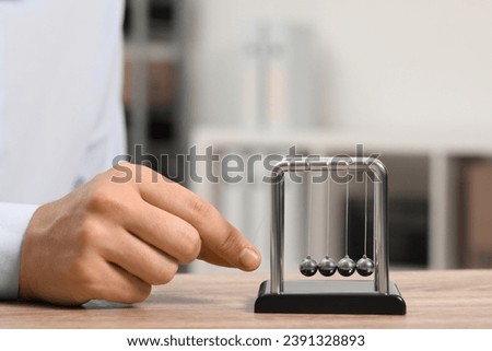 Man playing with Newton's cradle at table, closeup. Physics law of energy conservation