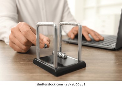 Man playing with Newton's cradle and using laptop at wooden table, closeup. Physics law of energy conservation