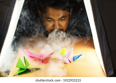 A Man Playing With Origami And Vaping Smoke