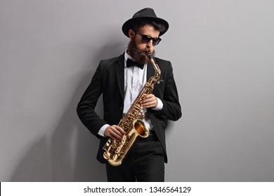 Man Playing A Sax And Leaning Against A Gray Wall