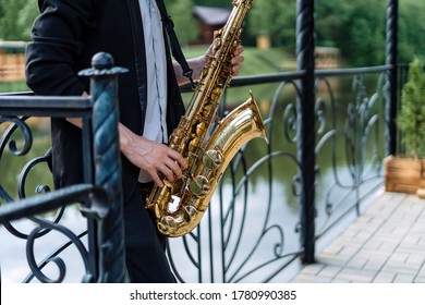 Man playing the saxophone, in the background is a beautiful lake. Beautiful fence and nature.