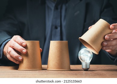 Man is playing a shell game by paper cups and reveals the right one that glowing light bulb is hiding, tips and tricks, good choice answer, find a creative idea - Shutterstock ID 2125133663