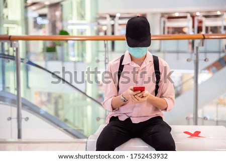 A man is playing a smartphone while sitting on a public shopping mall bench with caution social distancing signs. (Selective focus)