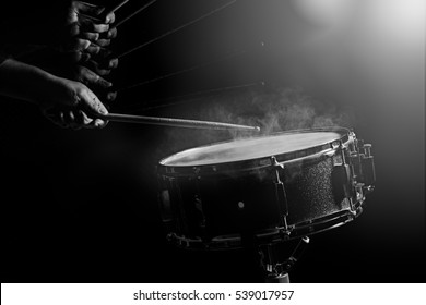 The man is playing snare drum in low light background.