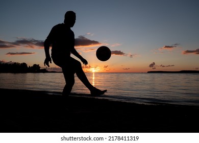 Man playing soccer on a beach at sunset. Dark evening view. Football player silhouette on a sandy beach late evening. - Powered by Shutterstock