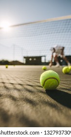Man playing tennis on a sunny day with tennis balls lying on the court. Close up of a tennis ball lying on the ground.