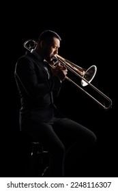 Man playing a trumpet and sitting on a chair isolated on black background